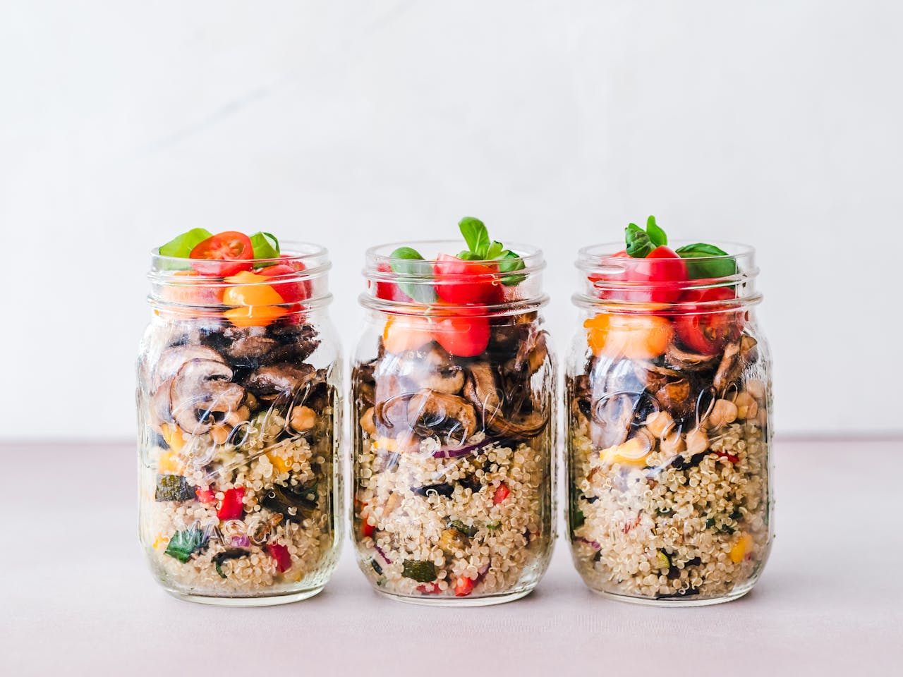 Services Three jars of colorful quinoa salad with mushrooms and tomatoes, perfect for a healthy meal.