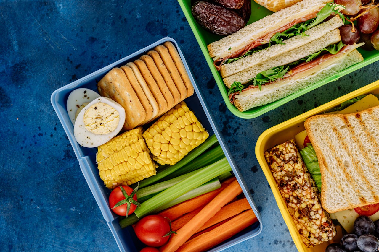Services Colorful lunchboxes featuring sandwiches, vegetables, and snacks for healthy eating.